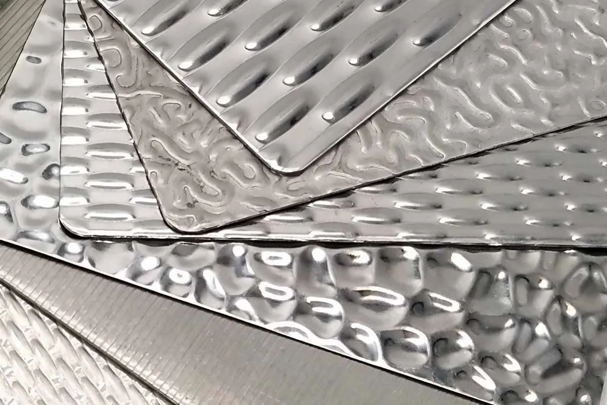 A close-up of different stainless steel patterned sheets stacked together, showing their metallic texture.
